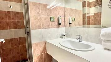 A modern bathroom with a white sink, a mirror, and a shower area.