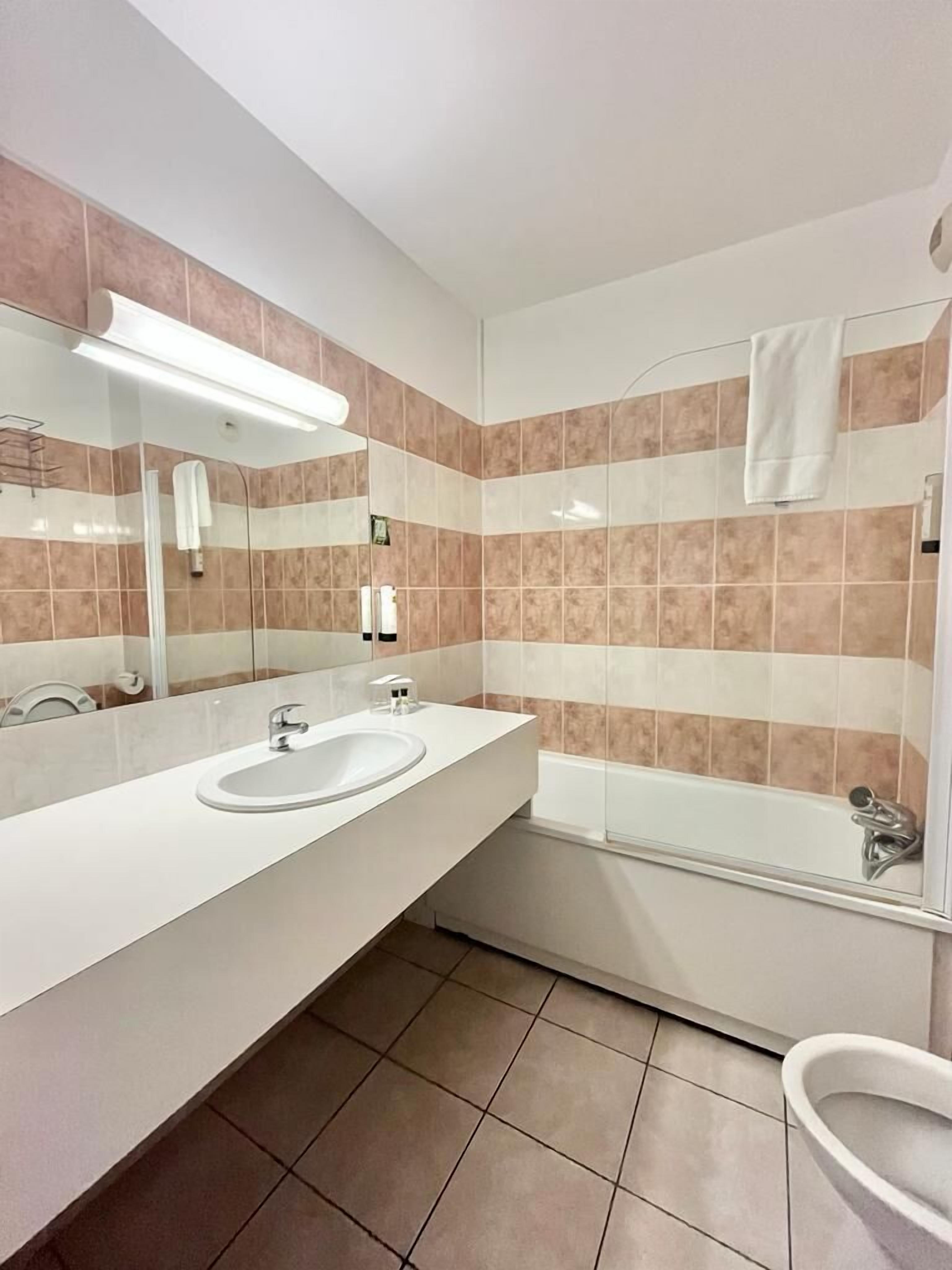 A modern bathroom with a large mirror, two sinks, a glass shower enclosure, and a toilet.