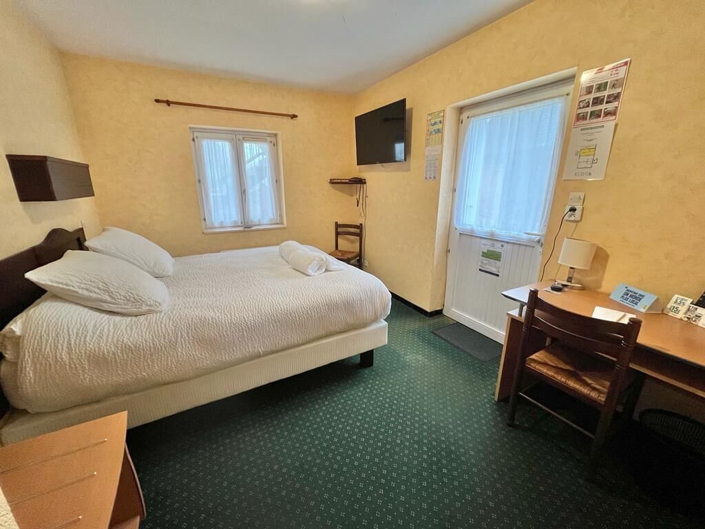 A hotel room with a bed, a desk, a chair, a TV, and a window.
