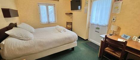 A hotel room with a bed, a desk, a chair, a TV, and a window.