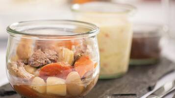 Eine Schüssel mit Eintopf, Gemüse und Fleisch, ein Glas Sahne und ein Gläscher Soße auf einer Schieferplatte.