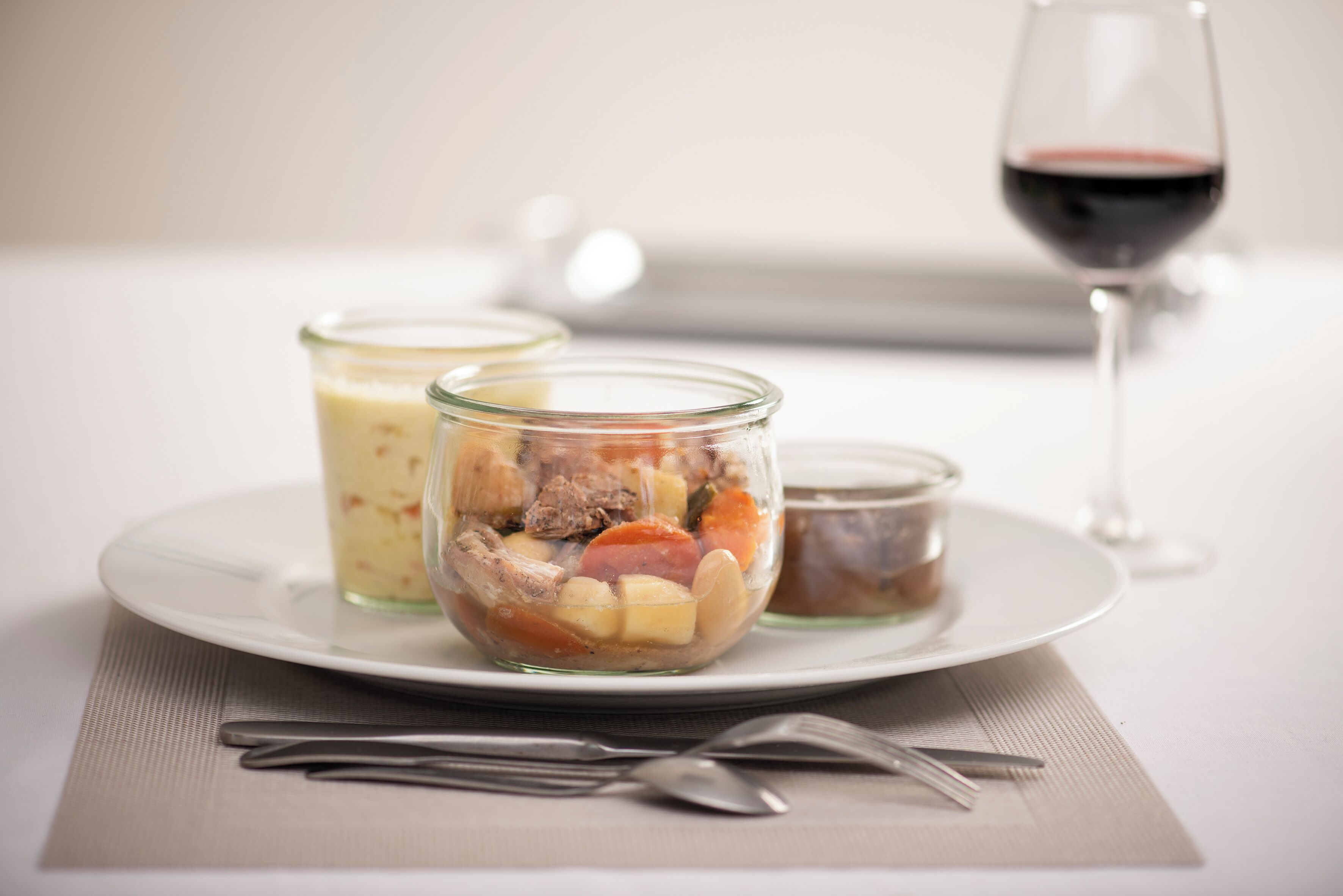 A plate with a food item, two glass containers, and a wine glass on a table.