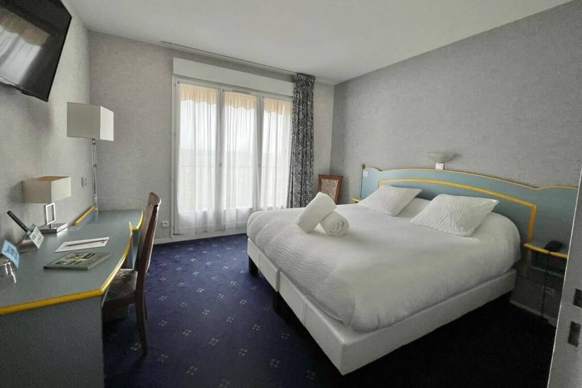 Ein Hotelzimmer mit einem Bett, einem Schreibtisch, einem Sessel, einem Fernseher und einem Fenster mit Vorhängen.