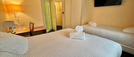 Habitación de hotel con dos camas, un televisor en la pared, un escritorio con lámpara y una puerta que da a otra habitación.