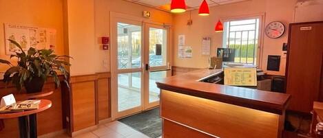 A reception area with a wooden counter, a potted plant, and a red pendant light.