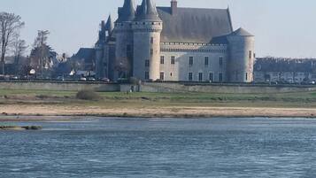 A large castle with multiple towers and a round tower, situated by a body of water.