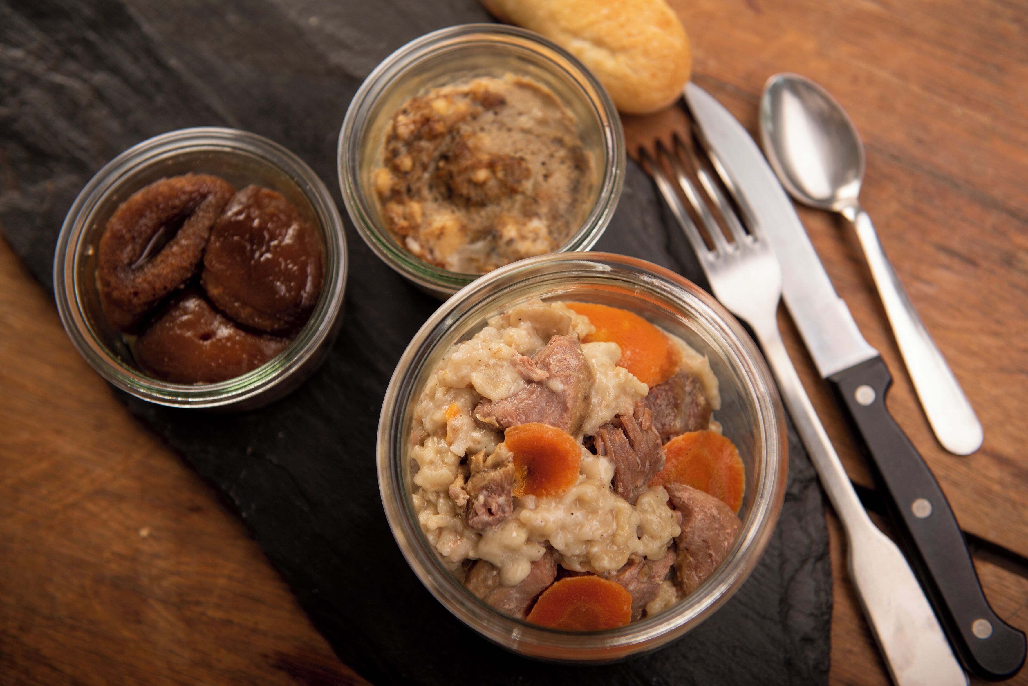 Three glass bowls of food on a dark slate surface with a knife and fork beside them.