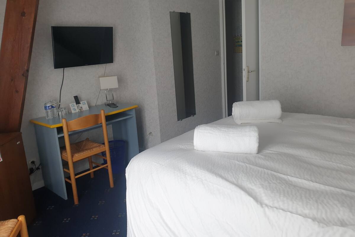 Ein Hotelzimmer mit Bett, Schreibtisch mit Stuhl, Flachbildfernseher, Spiegel und Tür.