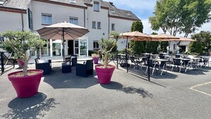 An outdoor seating area with tables and chairs, potted plants, and umbrellas. - Logis Hôtel Sully le Château (Saint-Père-sur-Loire)