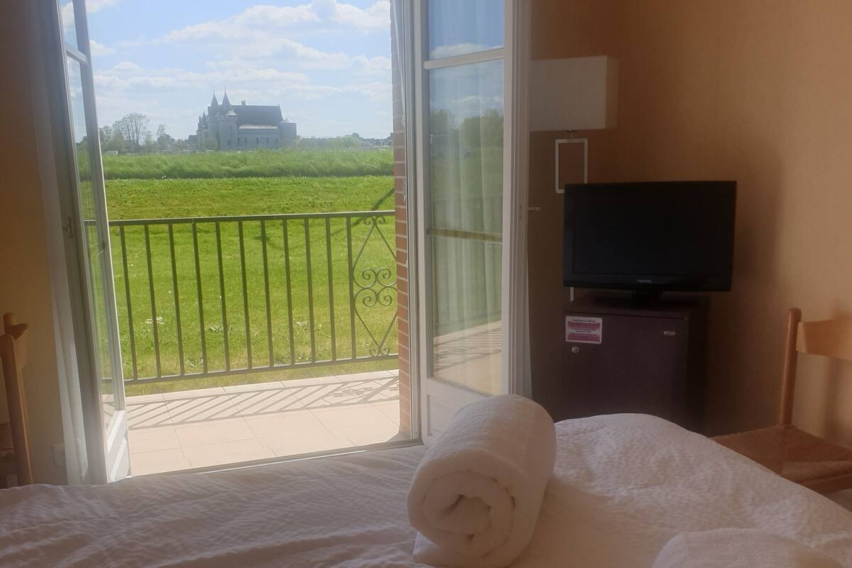 Ein Hotelzimmer mit Bett, zusammengelegtem Handtuch, Fernseher und Blick auf eine Burg vom Balkon aus.