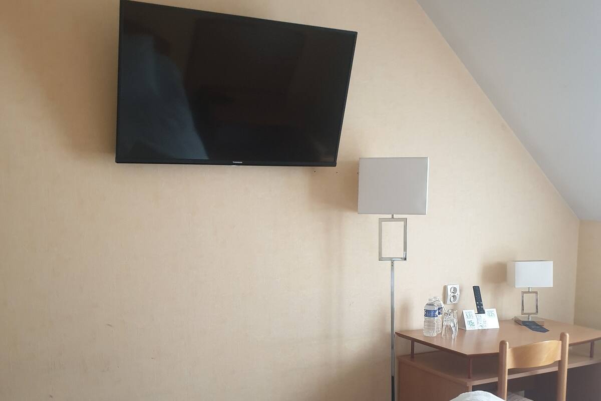 Ein Hotelzimmer mit einem Bett, zwei zusammengerollten Handtüchern, einem Schreibtisch mit Lampe, einem Fernseher und einem Sessel.