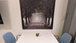 A white table with two blue chairs, a small potted plant, and a large black and white forest pathway artwork on the wall. - Fully Stocked Tampa Apartment (Tampa)
