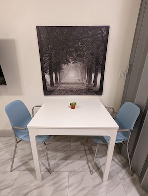 Relax in a stylish room with a white table, two chairs, and a framed tree-lined pathway print.