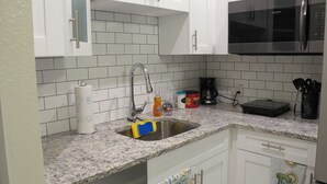 A kitchen with white cabinets, a stainless steel sink, a microwave, and various kitchen items on the countertop. - Fully Stocked Tampa Apartment (Tampa)