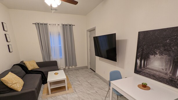 A modern living room with a sofa, a coffee table, a TV, and a dining area with a table and chairs. - Fully Stocked Tampa Apartment (Tampa)