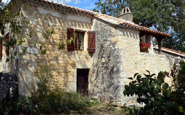 A rustic stone building with a tiled roof, a wooden door, and a window with shutters.
