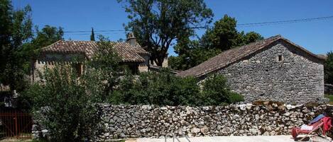 Un edificio de piedra con piscina, rodeado de un muro de piedra y vegetación.