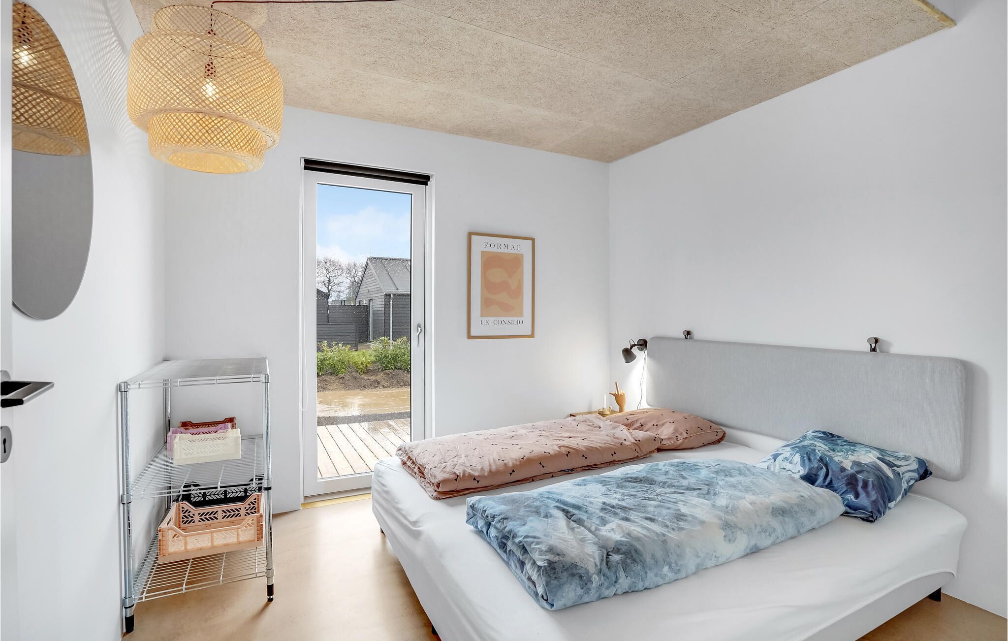 Ein Schlafzimmer mit Bett, Nachttisch, Lampe, einer Tür zu einem Balkon und einem an der Wand befestigten Regal mit Gegenständen.