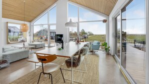 A spacious modern kitchen with large windows, a dining area with a long table, and a view of the outdoors. - 4 bedroom cozy home in Haderslev (Haderslev)