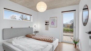 A modern bedroom with a large bed, a ceiling fan, a wall-mounted light, and a view through a glass door. - 4 bedroom cozy home in Haderslev (Haderslev)