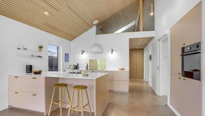 A modern kitchen with a central island, bar stools, a built-in oven, and a wooden ceiling. - 4 bedroom cozy home in Haderslev (Haderslev)