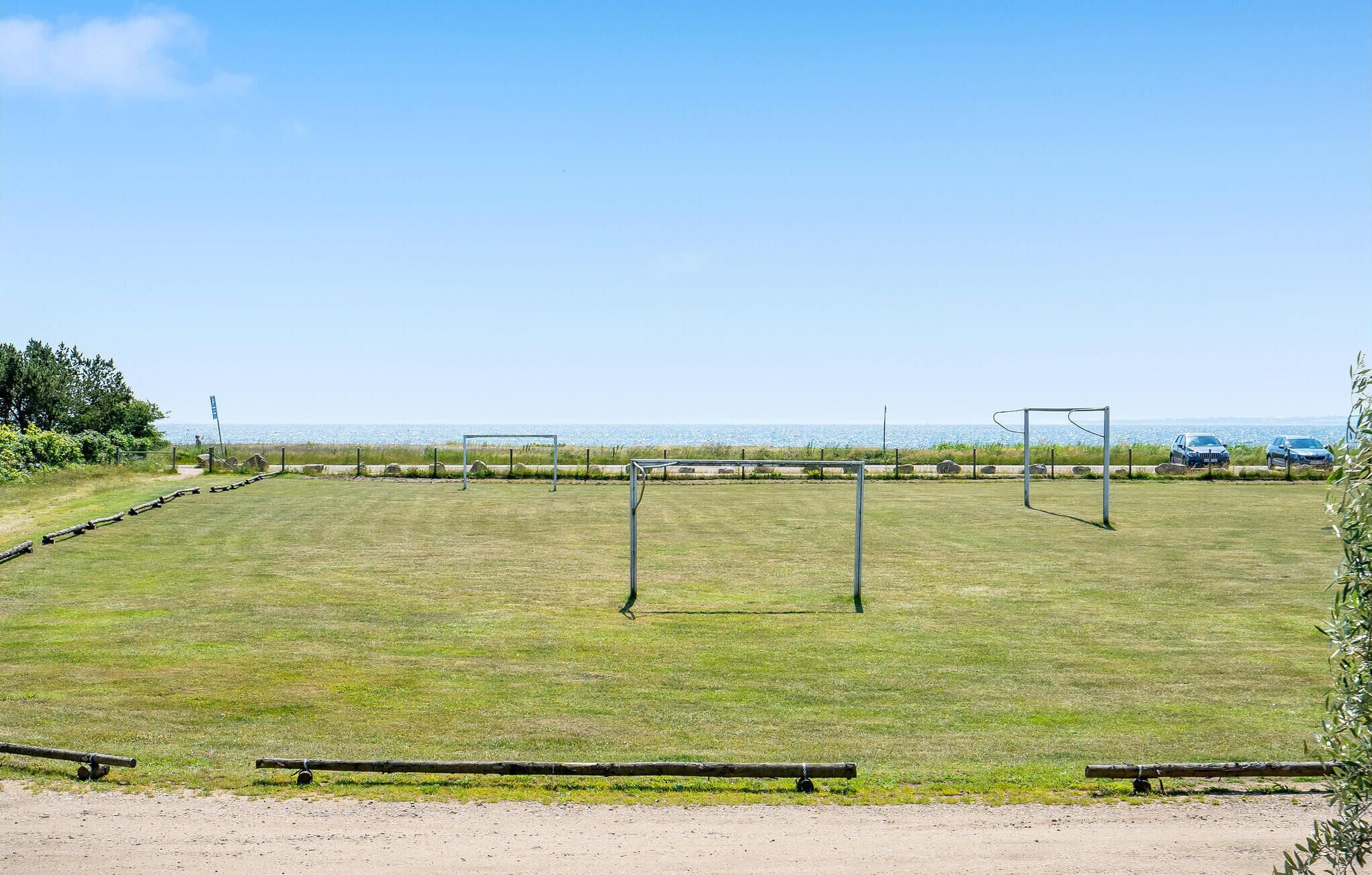 A grassy field with two soccer goals and a dirt path in the foreground.
