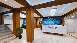 A reception area with a marble counter, wooden pillars, and a large aquarium. - Hotel Sea Port (Port Blair)