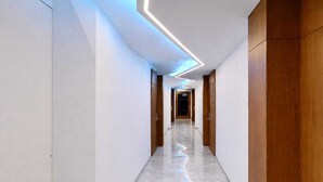 A modern hallway with a reflective floor, wooden doors, and a ceiling with linear lighting. - Hotel Sea Port (Port Blair)