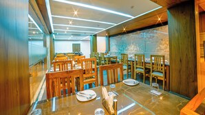 A restaurant with wooden furniture, marble tables, and a modern ceiling design. - Hotel Sea Port (Port Blair)
