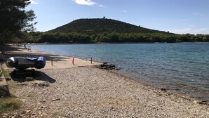 A pebble beach with a covered grill and a red kayak.