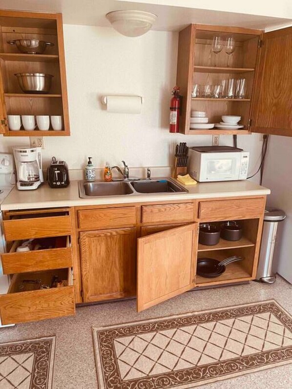 A compact kitchen with wooden cabinets, a microwave, a coffee maker, and a sink. - Lovely Clean Bright top floor unit Coin Op Laundry (Fairbanks)