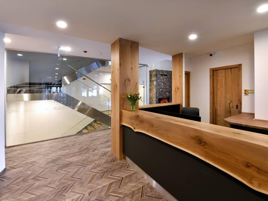 Un espace d’accueil doté d’un comptoir de réception en bois, d’une cheminée en pierre et d’un escalier menant aux étages supérieurs.