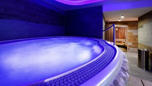 Un jacuzzi con techo iluminado en azul, una banca de madera y una pared de piedra.