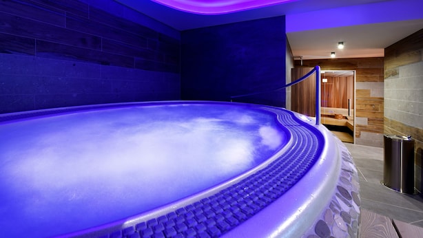 A hot tub with a blue-lit ceiling, a wooden bench, and a stone wall.