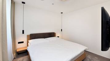 A modern bedroom with a bed, bedside tables, a wall-mounted TV, and pendant lights.