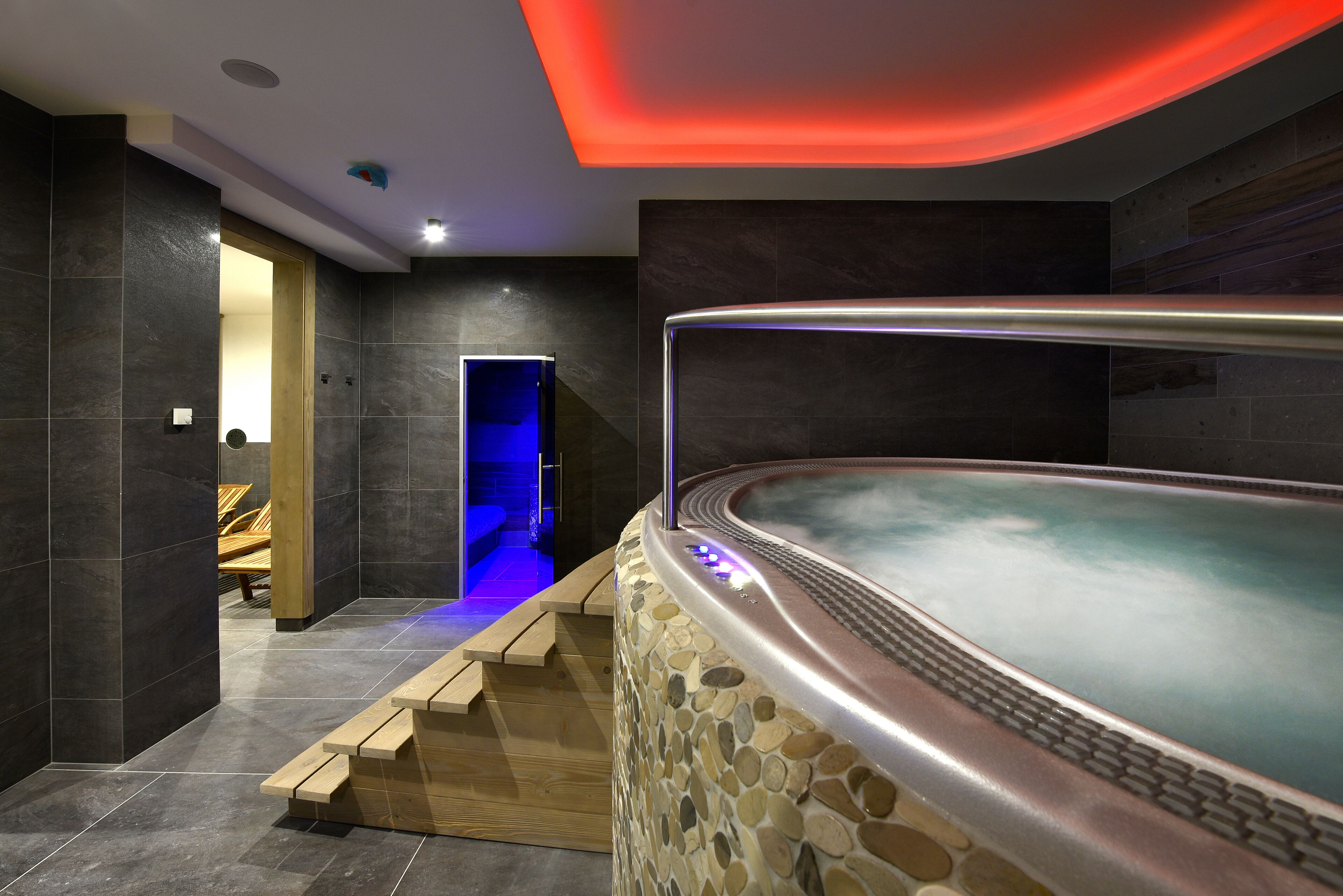 Un espace spa moderne avec un mur en pierre, un jacuzzi et des marches en bois menant à un espace de détente.