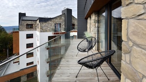 A balcony with two black chairs, a wooden deck, and a stone wall.