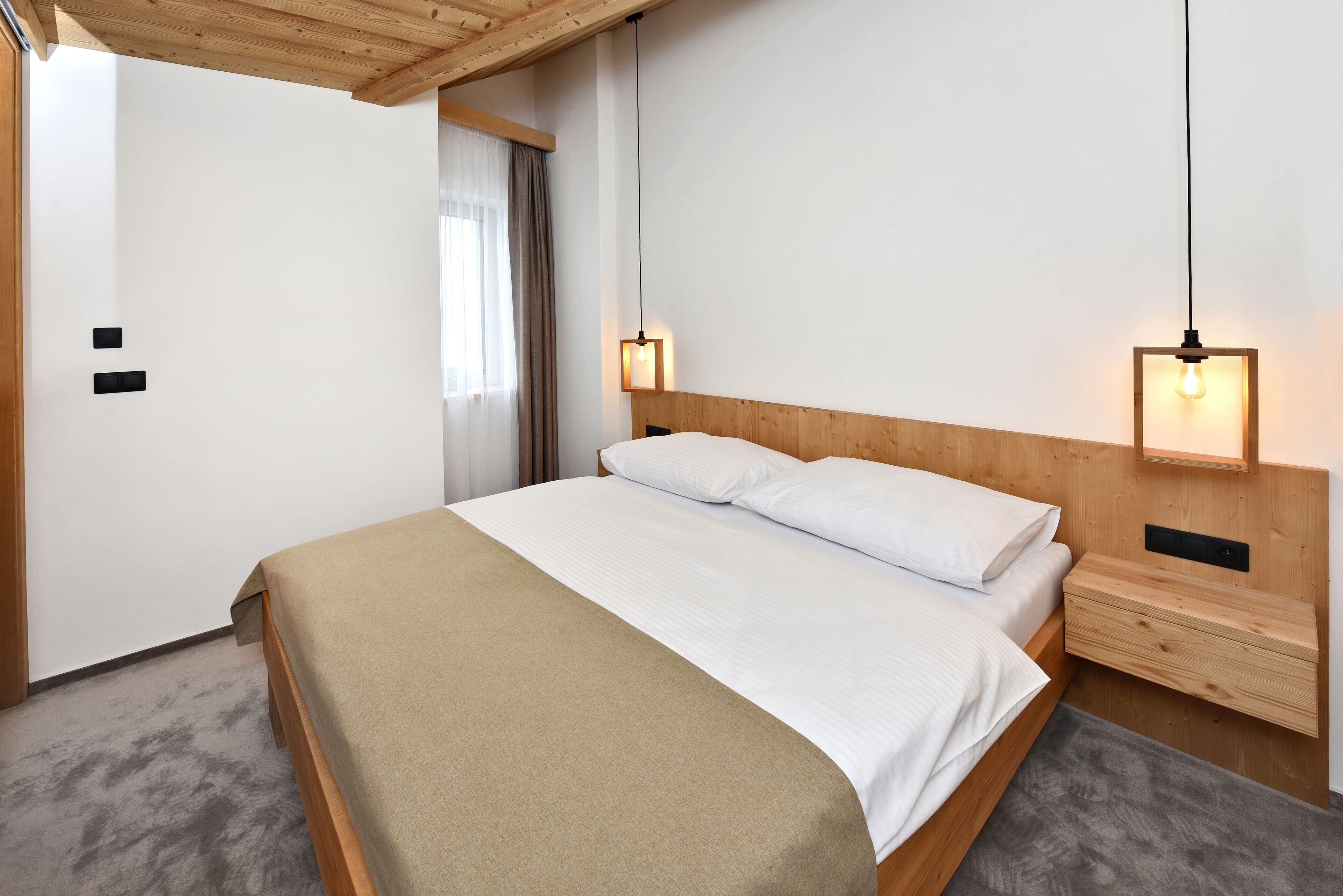 Un dormitorio con una cama de madera, dos mesitas de noche y techo de madera.