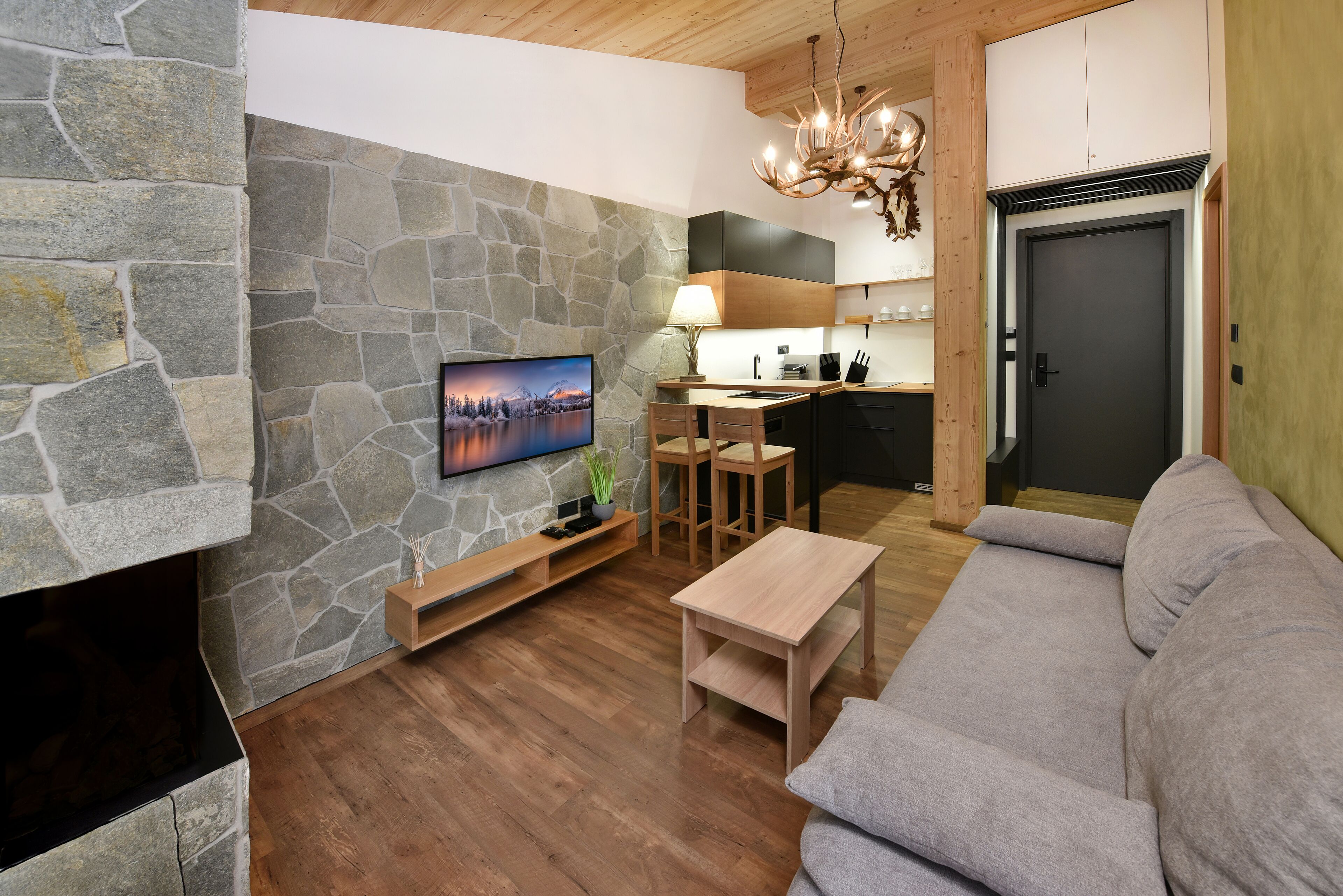 Ein modernes Wohnzimmer mit Kamin aus Stein, einem Flachbildfernseher, einem Holztisch und einem grauen Sofa.