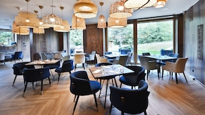A modern dining area with multiple tables and chairs, large windows, and hanging wicker light fixtures.
