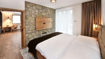 Quarto com parede de pedra, cama com roupa de cama branca, cabeceira de madeira e escrivaninha com cadeira.