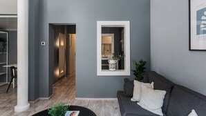 A modern living room with a grey wall, a framed mirror, a grey sofa, and a coffee table. - Unique 2BR Apartment in Filothei (Filothei-Psychiko)