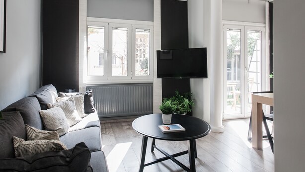 A modern living room with a grey sofa, a black coffee table, and a flat-screen TV mounted on the wall. - Unique 2BR Apartment in Filothei (Filothei-Psychiko)