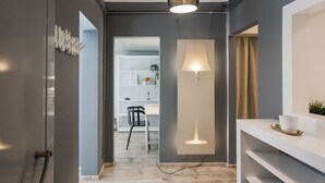 A modern interior with a grey wall, a white shelf with a lamp, and a door leading to a dining area. - Unique 2BR Apartment in Filothei (Filothei-Psychiko)