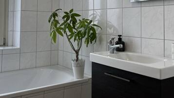 Ein modernes Badezimmer mit einer weißen Badewanne, einem Waschbecken mit schwarzem Seifenspender und einem Topfpflanzen.