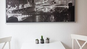 A dining area with a white table and chairs, a black and white cityscape photograph on the wall, and two small potted plants on the table. - Central apartment in Magdeburg with Netflix and kitchen WE18 (Magdeburg)