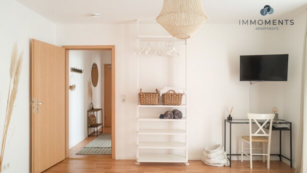 A modern apartment with a wooden door, a white shelving unit, a desk with a chair, and a television. - Central apartment in Magdeburg with Netflix and kitchen WE18 (Magdeburg)