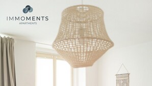A cozy room with a white chair, a small table, a hanging light fixture, and a window with curtains. - Central apartment in Magdeburg with Netflix and kitchen WE18 (Magdeburg)