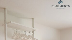 A room with a white shelving unit, a glass table with a chair, and a TV mounted on the wall. - Central apartment in Magdeburg with Netflix and kitchen WE18 (Magdeburg)