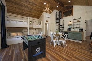 Um quarto acolhedor com mesa de pebolim, beliches, área de cozinha e escada.